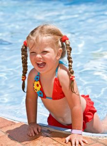 A youn girl in a red bikini smiles with joy while in a swimming pool.