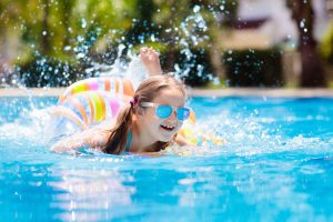 Picture of a young girl swimming in a pool with goggles and a float.