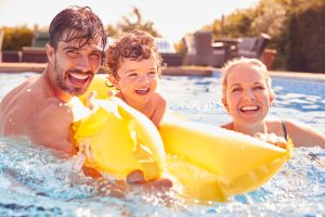Picture of a father, mother, and son playing in a swimming pool with a yellow float.