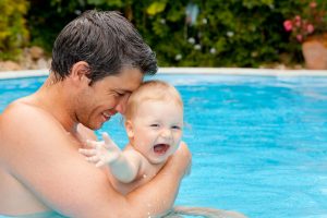 A father and his baby play in a swimming pool